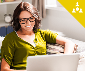 A young woman wearing glasses sitting on a coach with a laptop