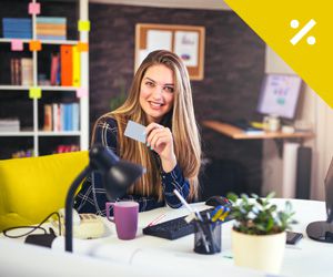 A young woman sitting at a desk holding a credit card smiling