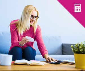 A young woman sitting on a couch and holding a piece of paper while operating a calculator.