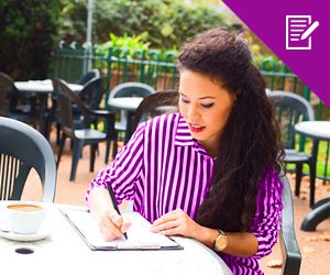 A young woman sitting on a table writing notes and having coffee