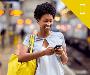 A young woman standing and smiling while using a smartphone