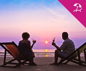 A couple having a cocktail while sitting on the beach during a sunset